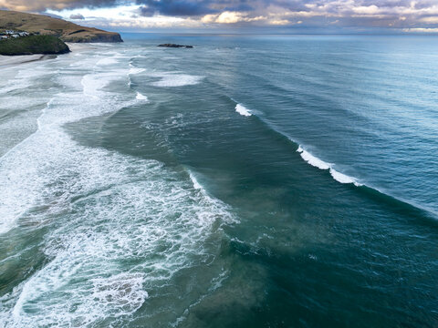 Aerial view of the coastline with rolling waves breaking on the sandy beach under a cloudy sky in Dunedin, Otago Region, New Zealand.