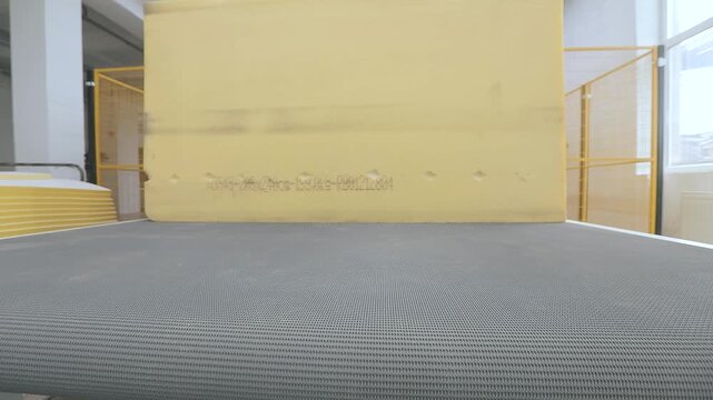An automated CNC foam-cutting machine processes a large block of polyurethane foam in a modern manufacturing facility. A factory producing mattresses and upholstered furniture. Foam-cutting machine