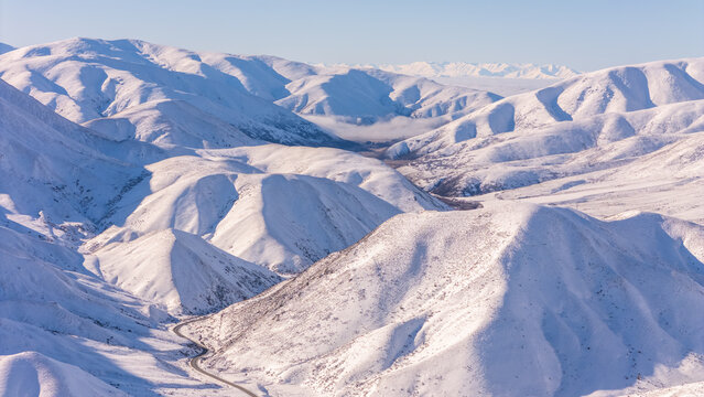 Aerial view of Lindis Pass featuring snow-covered mountain ranges and a winding road through the winter landscape in Otago Region, New Zealand.