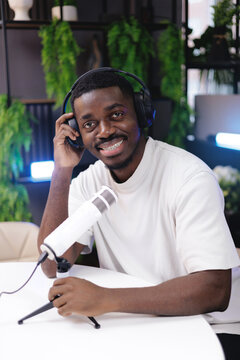 Portrait Young african male podcaster smiling with headphones and microphone in modern studio for video blog or podcast