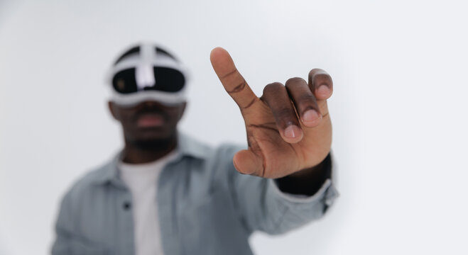Closeup gesture with finger to press button. African adult male engaging with virtual reality using headset on white studio background