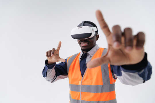 African male in safety uniform using vr headset on white background, touching immersive display in industry technology