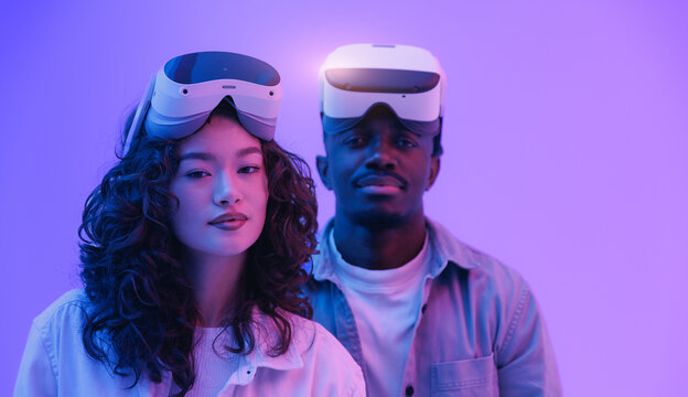 Multiethnic team Young asian female and african male with vr headsets in futuristic setting with neon light and sunlight