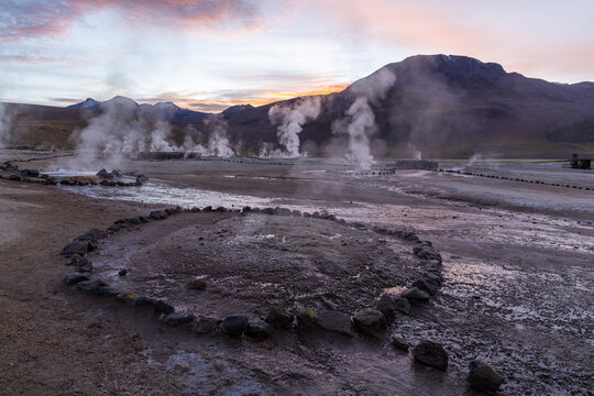 View of El Tatio geysers with rising steam plumes against a backdrop of volcanic mountains at sunrise in the Antofagasta, Chile.