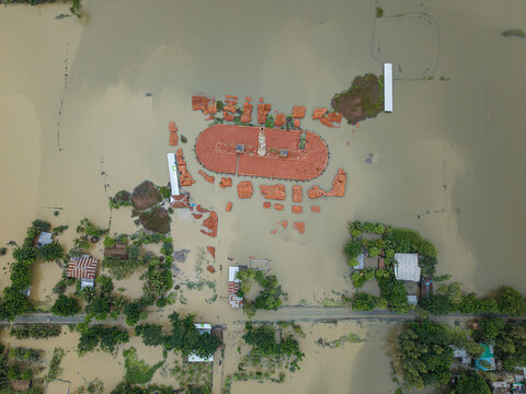 Banshkhali Upazila, Bangladesh - 10 July 2026: Aerial view of a flooded rural landscape with partially submerged brick structures and a kiln surrounded by brown floodwaters.