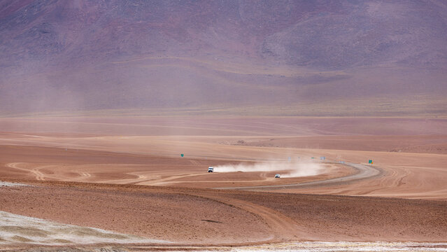 View of vehicles driving on a dusty dirt road through the vast arid Atacama desert landscape of Chile.