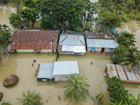Banshkhali Upazila, Bangladesh - 10 July 2026: Aerial view of flooded houses and residential buildings surrounded by rising floodwaters with people wading through the water.