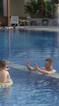 Father and two young brothers laugh while spraying water at each other with colorful water blasters in swimming pool. Family bonding, joyful childhood and unforgettable summer memories concept