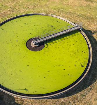 Aerial view of a circular secondary clarifier at a wastewater treatment plant covered with green algae, featuring a metal bridge mechanism in Le Pouzin, Auvergne-Rhone-Alpes, France.