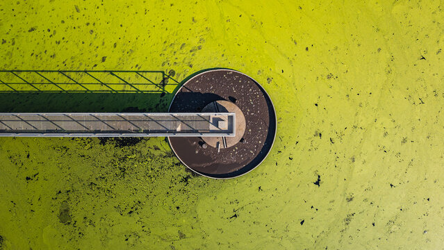 Aerial view of a circular secondary clarifier at a wastewater treatment plant covered with green algae, showcasing water treatment infrastructure in Le Pouzin, Auvergne-Rhone-Alpes, France.