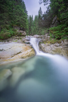 View of Zadna Javorova dolina waterfall with smooth flowing water over rocks surrounded by dense pine forest in High Tatras National park, Tatranska Javorina, Presovsky kraj, Slovakia.