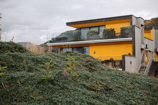 Modern yellow house with glass balcony overlooking a green hillside in Norway