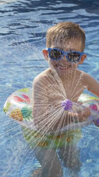 Little boy sprays water with colorful water blaster near swimming pool on sunny day. Outdoor water games, active summer childhood and joyful vacation concept. 