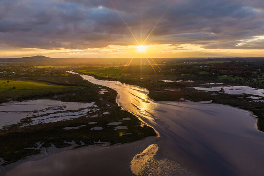 Aerial view of the Lower King river winding through wetlands and fields at sunset with a sunburst effect in the sky in Lower King, Western Australia, Australia.