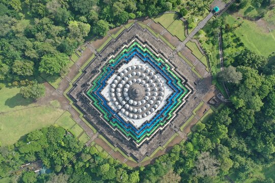 Aerial view of Borobudur Temple, a massive Buddhist monument with symmetrical stone stupas surrounded by lush green trees and parkland in Borobudur, Central Java, Indonesia.