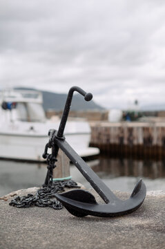 Nautical anchor with heavy chain rests on a stone pier by the water