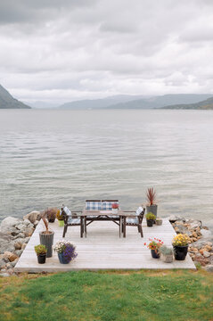 Outdoor dining set on a wooden deck by a calm Norwegian fjord