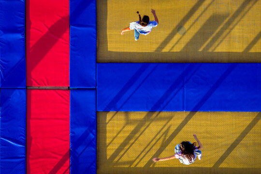Aerial view of two people jumping on a trampoline with vibrant blue and red safety padding, casting long shadows in Belgrade, City of Belgrade, Serbia.