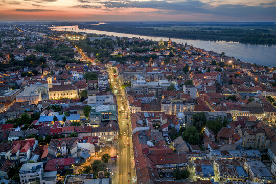 Aerial view of the historic Zemun district at sunset, featuring traditional red-tiled rooftops, the Danube river, and illuminated streets in Belgrade, City of Belgrade, Serbia.
