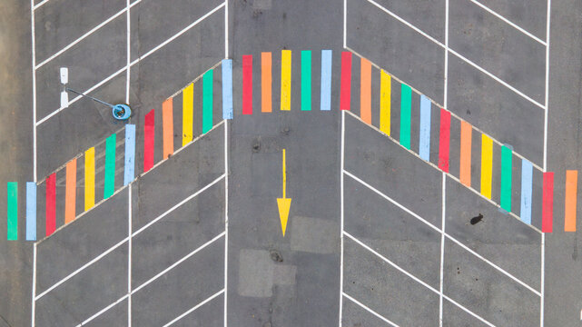 Aerial view of a rainbow-colored pedestrian crossing painted on the asphalt of a parking lot with white markings and a yellow directional arrow in Reykjavik, Reykjavikurborg, Iceland.