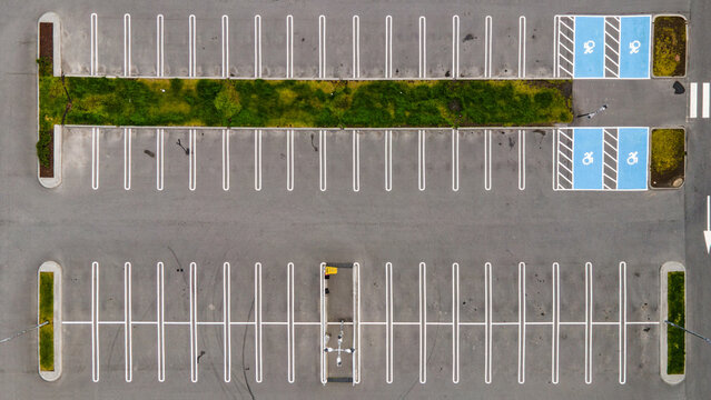 Aerial view of a parking lot with marked spaces, blue accessible parking spots, a central green strip, and an electric vehicle charging station in Reykjavik, Reykjavikurborg, Iceland.