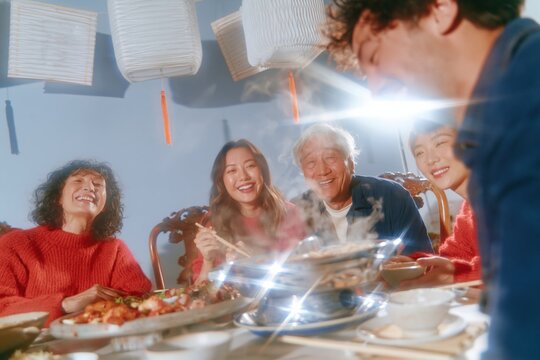 Happy Asian family laughing around a steaming hot pot for a Lunar New Year reunion dinner with glowing lanterns and festive red knitwear
