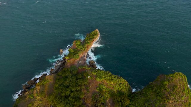 Aerial view of Baron Beach rocky cliff with lush vegetation and crashing waves along the coastline in Tanjungsari, Special Region of Yogyakarta, Indonesia.
