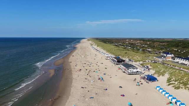 Aerial view of the sandy beach with rows of blue and white beach huts, dunes, and a restaurant along the coastline in De Koog, North Holland, Netherlands.