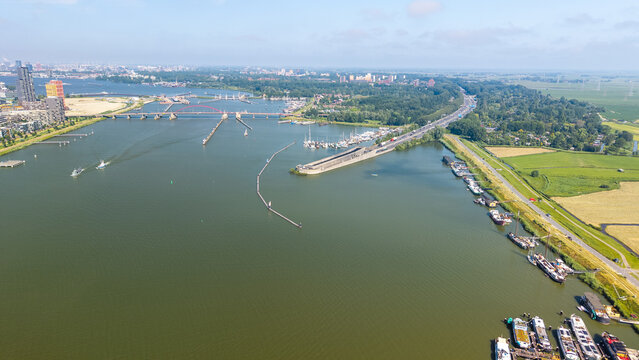 Aerial view of the IJ river with boats docked along the waterfront, modern bridges, and urban landscape in Amsterdam, North Holland, Netherlands.
