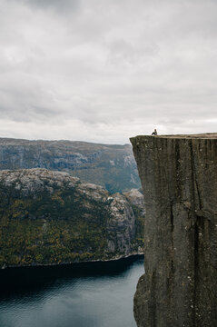 Person sitting on the edge of a dramatic cliff overlooking a Norwegian fjord