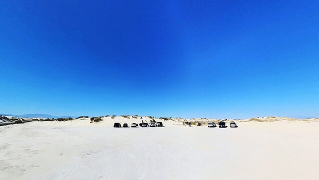 View of White Sands National Park with cars parked on the white gypsum sand dunes under a clear blue sky in New Mexico, United States.