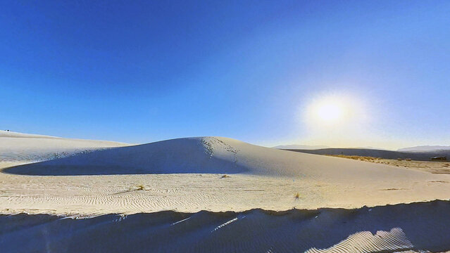 View of White Sands National Park featuring vast white gypsum sand dunes under a bright sun and clear blue sky in New Mexico, United States.