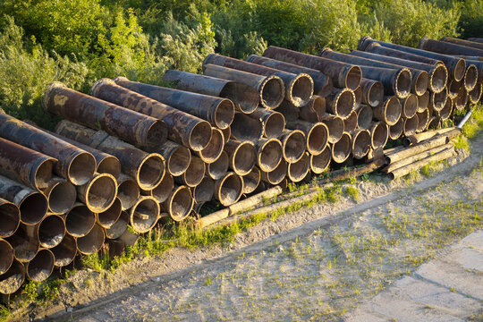 Aerial view of a large stack of industrial metal pipes resting on a dirt ground near green vegetation, Krakow, Lesser Poland Voivode, Poland.
