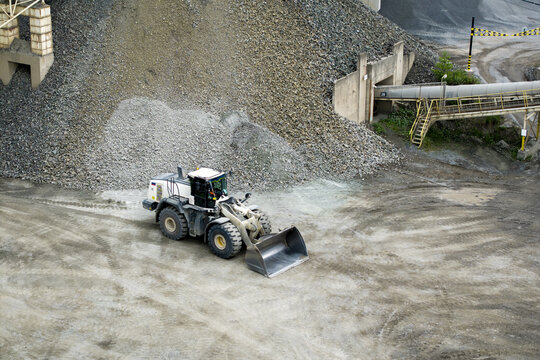 Aerial view of a wheel loader operating at a gravel quarry with large piles of crushed stone and industrial conveyor systems in Krakow, Lesser Poland Voivode, Poland.