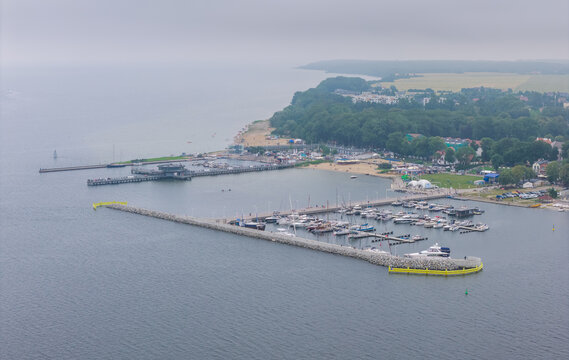 Aerial view of Puck Bay marina with sailboats and yachts docked at the stone breakwater, surrounded by the coastline and greenery in Puck, Pomeranian Voivodeshi, Poland.