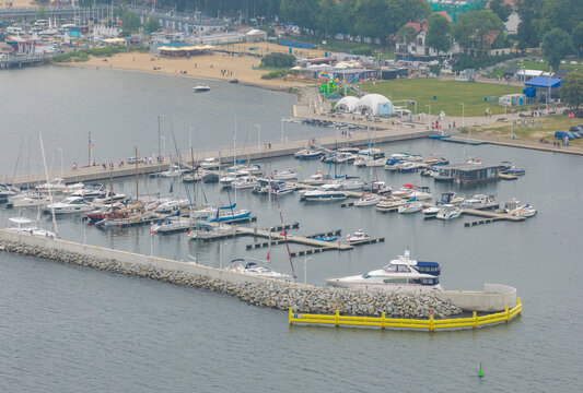 Aerial view of Puck Bay marina with numerous sailboats and yachts docked at the pier, sandy beach, and coastal park area in Puck, Pomeranian Voivodeship, Poland.