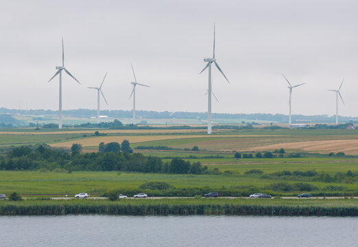 Aerial view of wind turbines in fields near the coast of Puck Bay with cars driving on a road in Puck, Pomeranian Voivodeshi, Poland.