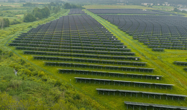 Aerial view of a large solar farm with rows of photovoltaic panels installed on a green field in Zarnowiec, Pomeranian Voivodeship, Poland.