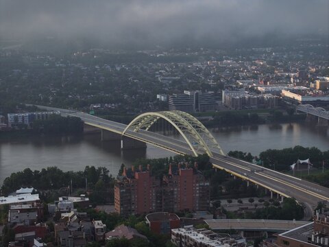 Cincinnati, United States - 12 July 2026: Aerial view of the Daniel Carter Beard Bridge spanning the Ohio River, surrounded by urban buildings and lush greenery under a cloudy sky.
