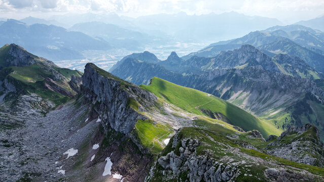 Aerial view of Cornettes de Bise with rugged limestone peaks, lush green alpine slopes, rocky terrain, and patches of snow in La Chapelle-d'Abondance, Auvergne-Rhone-Alpes, France.