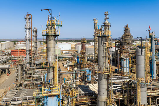 Aerial view of an industrial oil refinery with tall distillation towers, complex piping systems, and storage tanks under a clear sky in United Kingdom.