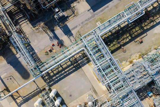 Aerial view of an industrial refinery complex featuring an intricate network of metal pipes, steel infrastructure, and storage tanks under clear daylight in the United Kingdom.