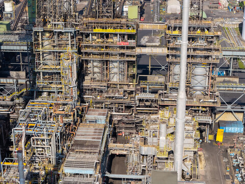 Aerial view of a large industrial refinery complex with intricate networks of metal pipes, tall processing towers, and complex infrastructure in the United Kingdom.