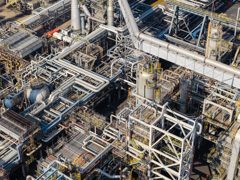 Aerial view of an industrial oil refinery complex featuring intricate networks of steel pipes, large storage tanks, and metal scaffolding under bright daylight in the United Kingdom.