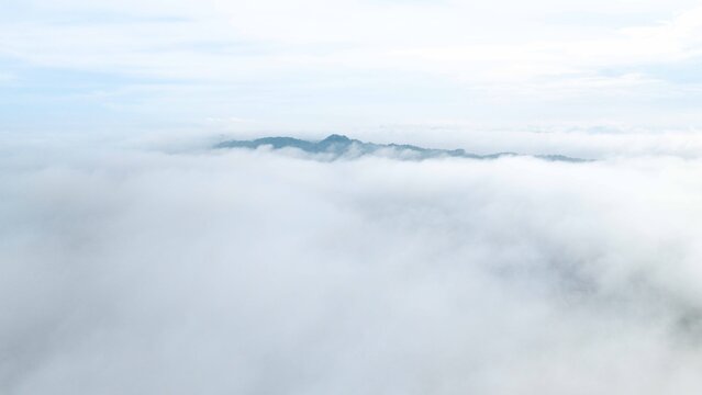 Aerial view of mountain peaks emerging above a dense layer of white clouds under a bright sky in the Philippines.