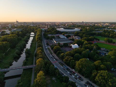 Hanover, Lower Saxony, Germany - 12 July 2026: Aerial view of Maschsee lake, lush trees, the Heinz von Heiden Arena, and a park area with a white stage at golden hour.