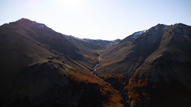 Aerial view of a mountain valley in the Andes with a winding stream, rugged slopes, and autumn foliage in Coyhaique, Aysen, Chile.