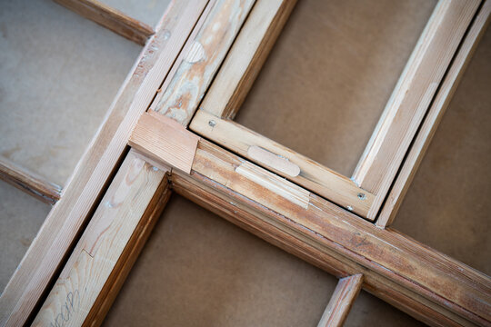 Antique window frame at worktable in restoration workshop undergoing renovation and reconstruction, stage of restoring wooden transom, insertion of patches made of wood same species, hardness and age.
