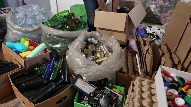 Hands sorting recyclable materials into labeled recycling bins for plastic, paper, glass, metal, and electronics. Waste separation and circular economy concept