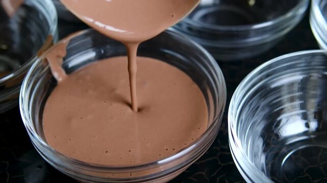 Chocolate pudding poured into glass dessert cups with ladle during homemade dessert preparation close up